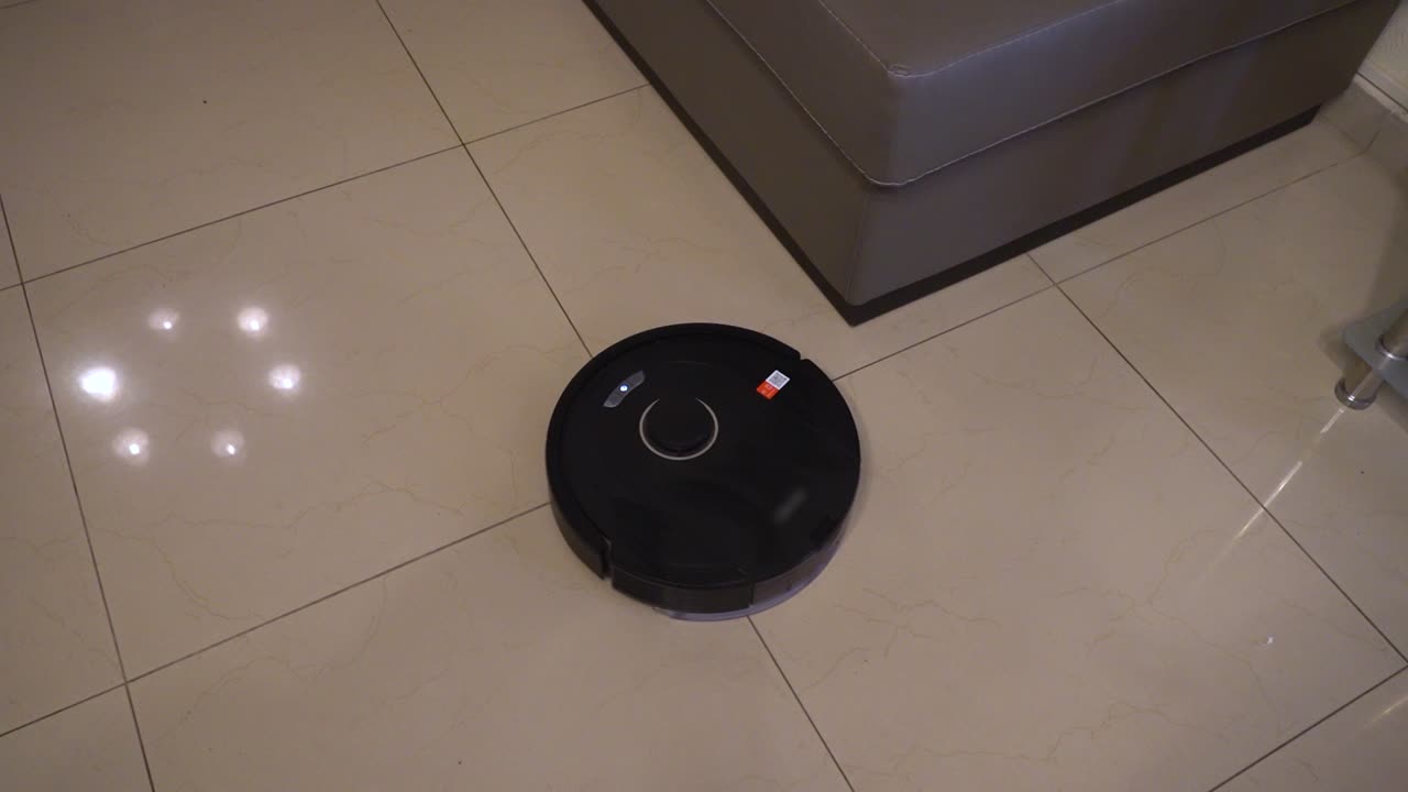 Un mocio robotizzato opera su pavimenti piastrellati in una casa moderna. Si muove tra i mobili, pulendo efficacemente polvere e sporco, mostrando le sue funzionalità automatizzate e il design in azione.