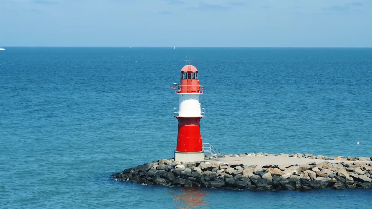 Nærbillede af et rød-hvidt fyrtårn på en bølgebryder af sten ved Warnemünde i Rostock, Tyskland, stående mod det rolige blå Østersø på en solrig sommerdag