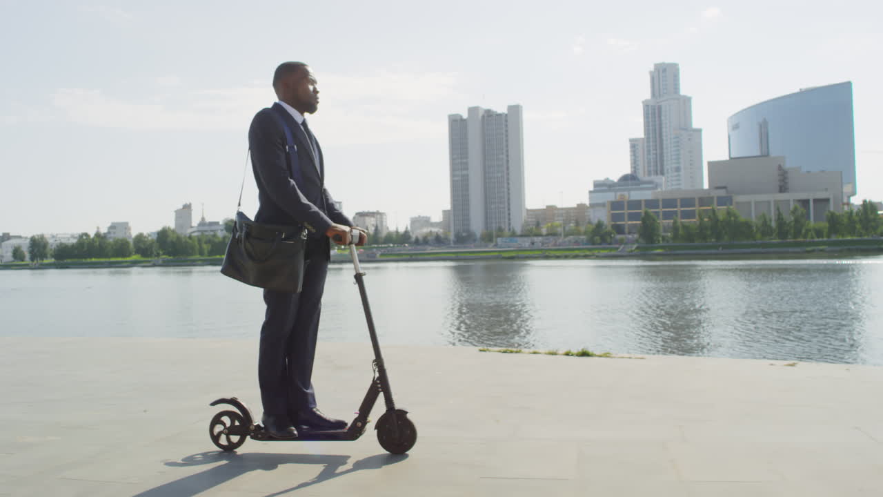 Black Businessman Riding On E-Scooter Along River