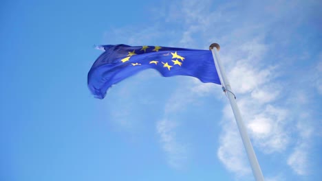 looking up the eu flag waving on its own in strong wind on a blue and cloudy sky, symbol of the european union alliance