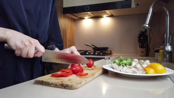 Donna in accappatoio blu che taglia i pomodori su un tagliere di legno in cucina