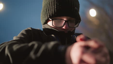 blurred close-up of a young boy wearing glasses and a black jacket, resting on an iron bar with his head bowed and headphones around his neck