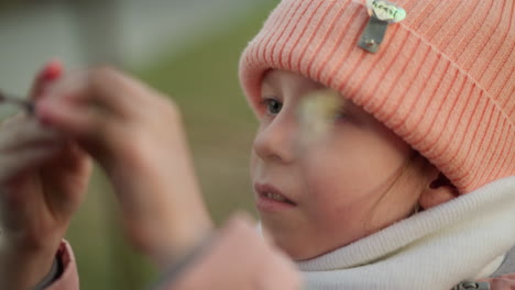 close-up of a little girl dressed in a pink jacket and beanie, intently examining and touching a dry tree branch. her focused expression captures a moment of curiosity and wonder