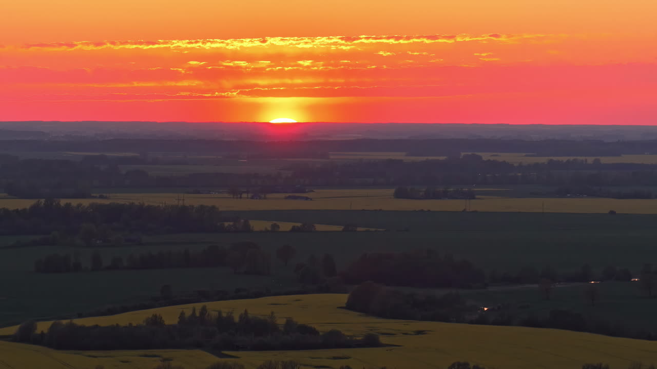 A vivid red sky glows at sunrise or sunset behind a serene landscape in a pedestal shot.