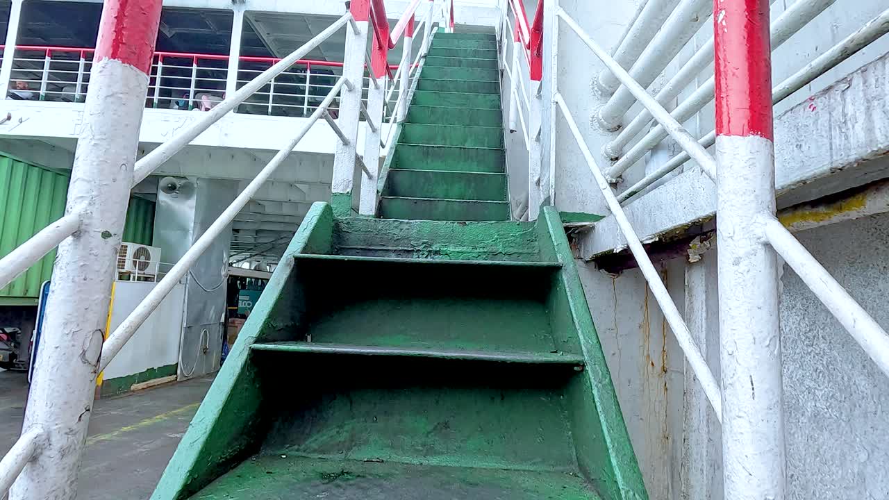 A sequence of green stairs with red railings on a ferry in Koh Samui, captured under natural daylight