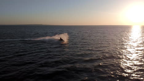 a woman on a jet ski splashes through waves on an open ocean during sunset