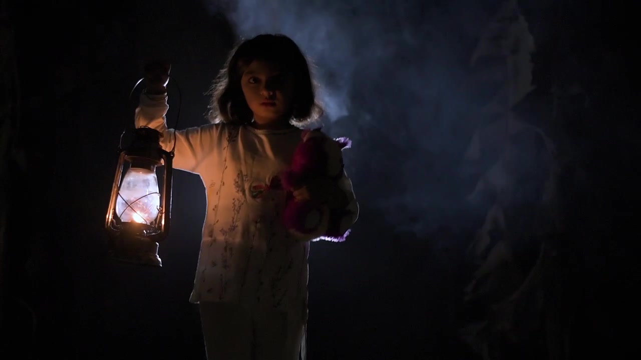 Una bambina sola cammina attraverso una foresta nebbiosa e brumosa di notte con una lanterna in inverno