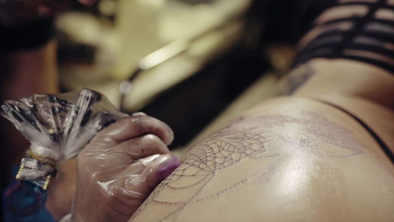 татуировщик работает над дизайном паучиной татуировки