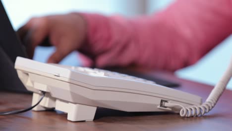 close up view of a hand attending handset telephone while typing in laptop