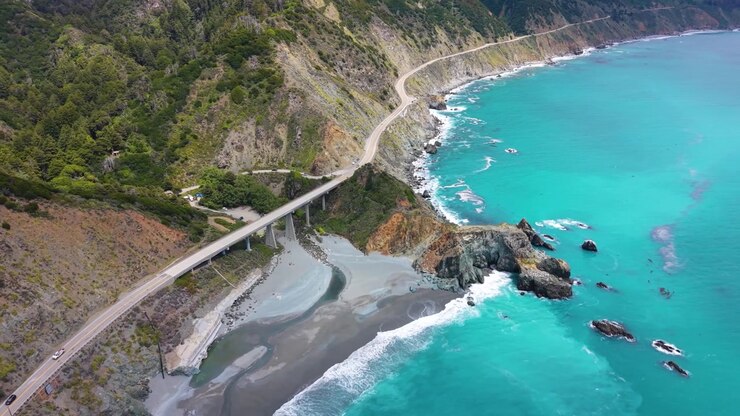 Vista aerea con drone dell'iconico Ponte Bixby Creek che attraversa un canyon lungo la Highway 1 con acqua oceanica turchese sottostante