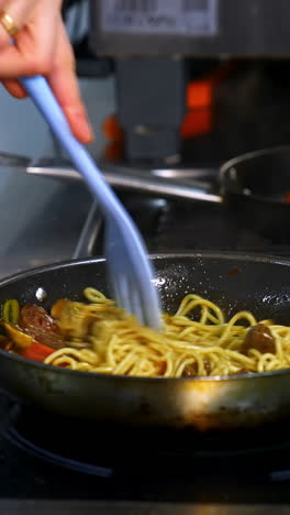 cooking and stirring the spaghetti with red tomatoes and mushrooms in the frying pan. video from a side. vertical video