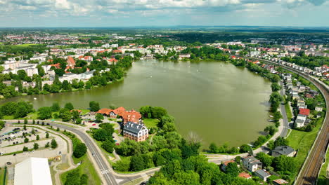 Aerial-view-of-Iława,-featuring-a-large-lake-surrounded-by-residential-buildings-and-greenery-under-a-partly-cloudy-sky