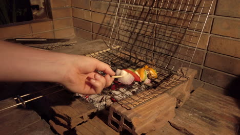 handheld shot of man removing vegetable kebabs from charcoal bbq grill at night