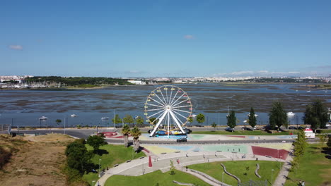 Vista-Aérea-De-La-Rueda-De-La-Fortuna,-El-Parque-De-La-Ciudad-Y-La-Ciudad-De-Seixal-Del-Estuario-En-Un-Día-Soleado-De-Verano-En-Portugal