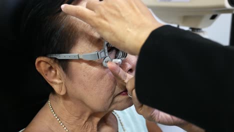 usando un marco de prueba, una anciana se está haciendo revisar los ojos manualmente en una tienda óptica en bangkok, tailandia