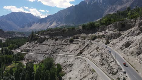 aerial view of hunza valley, pakistan, road under mountains on sunny summer day, drone shot