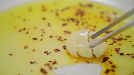 closeup tweezers moves a fresh garlic, frying in pan with hot chilli in oil