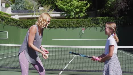 madre caucásica enseñando a su hija a jugar al tenis en la cancha de tenis en un brillante día soleado