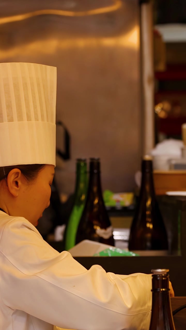 Chef donna asiatica in uniforme bianca e cappello prepara il cibo al bancone della cucina a Tokyo