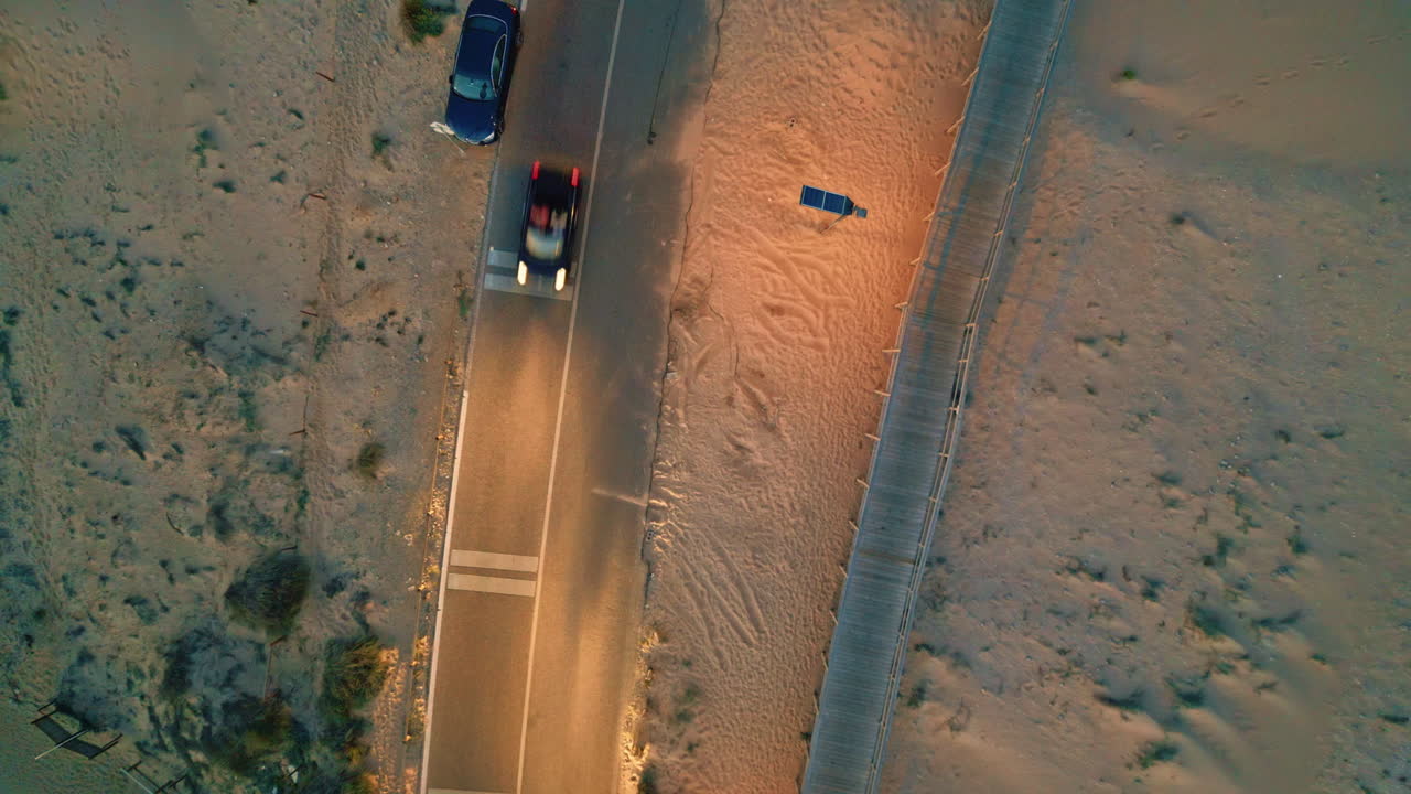 Cars riding desert road with headlights turning on at summer evening top view.