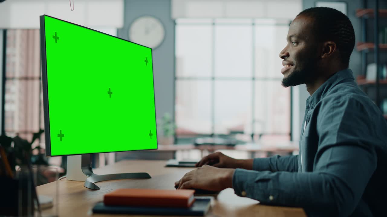 Handsome Black African American Specialist Working on Desktop Computer with Green Screen Mock Up Display at Home Living Room. Freelance Man Chatting to Clients Over the Internet on Social Networks.