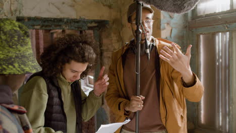 three production coworkers talking while reading a document and holding a microphone during recording of a movie in a ruined building 1