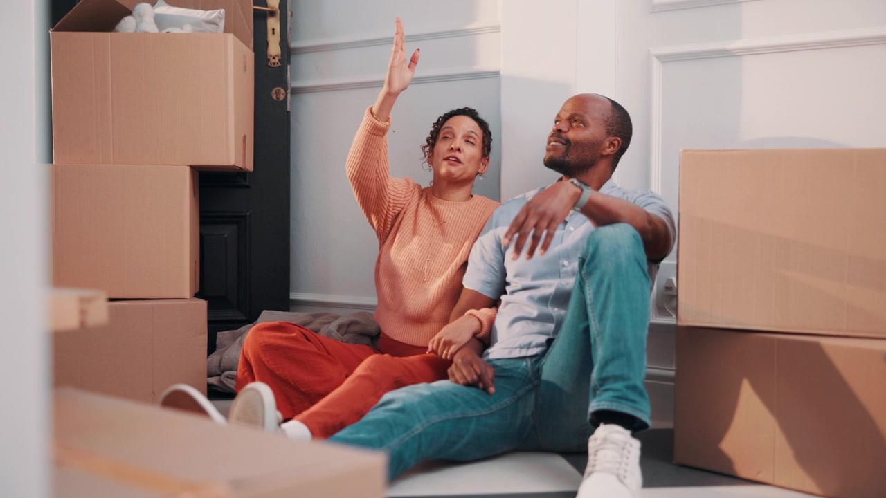 Couple Sitting on Floor Surrounded by Moving Boxes in New Home