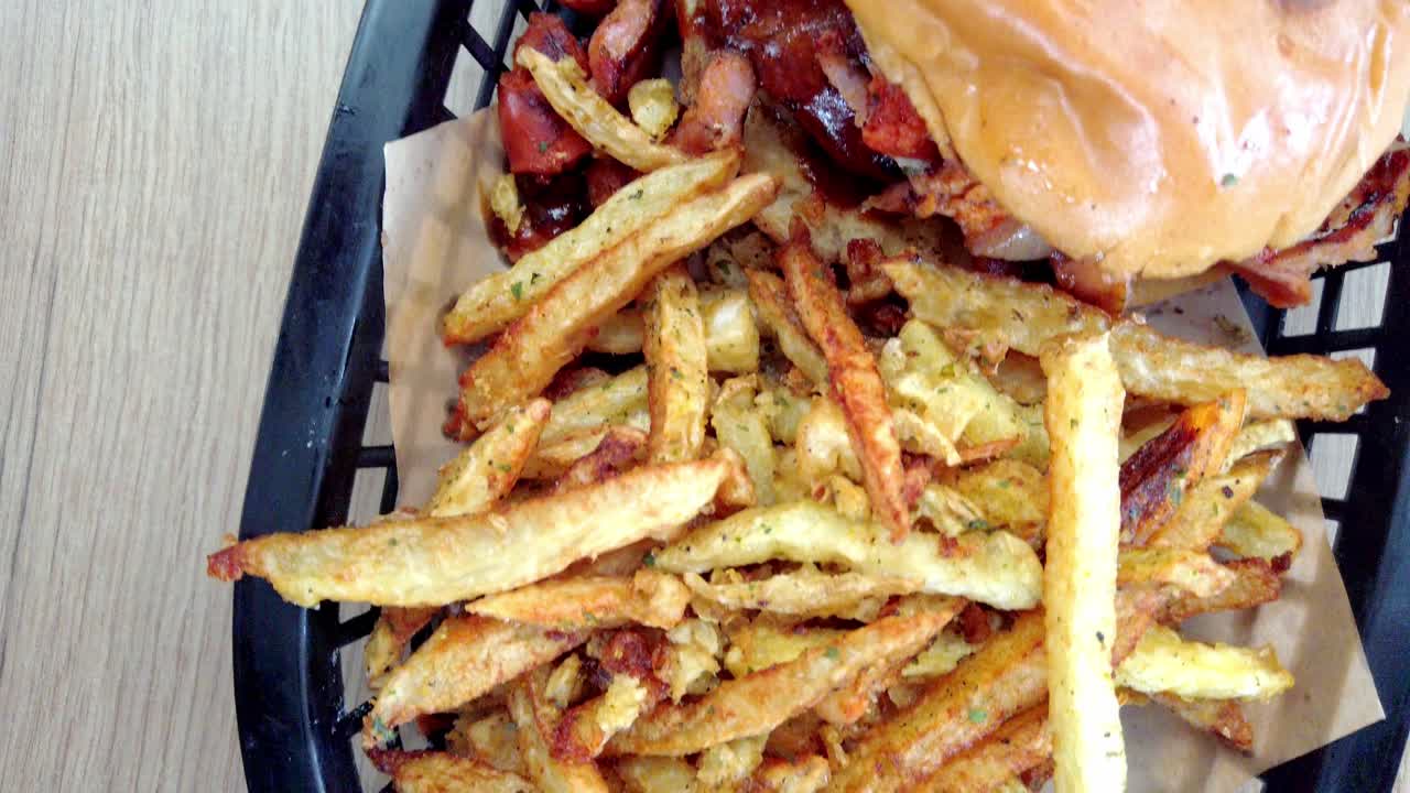 Top view close up of gourmet burger with sausage, meat, and fries served in black basket