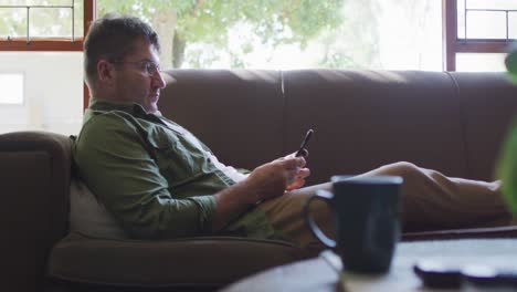 Caucasian-man-sitting-on-sofa,-using-smartphone-at-home