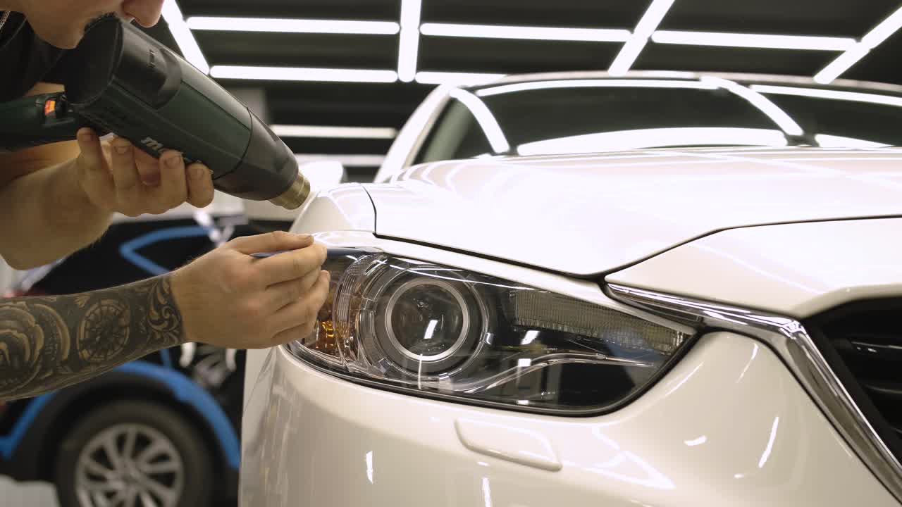 hombre cubriendo el coche con cinta de poliuretano de vinilo. películas para el coche. pegatina película protectora en el faro del coche