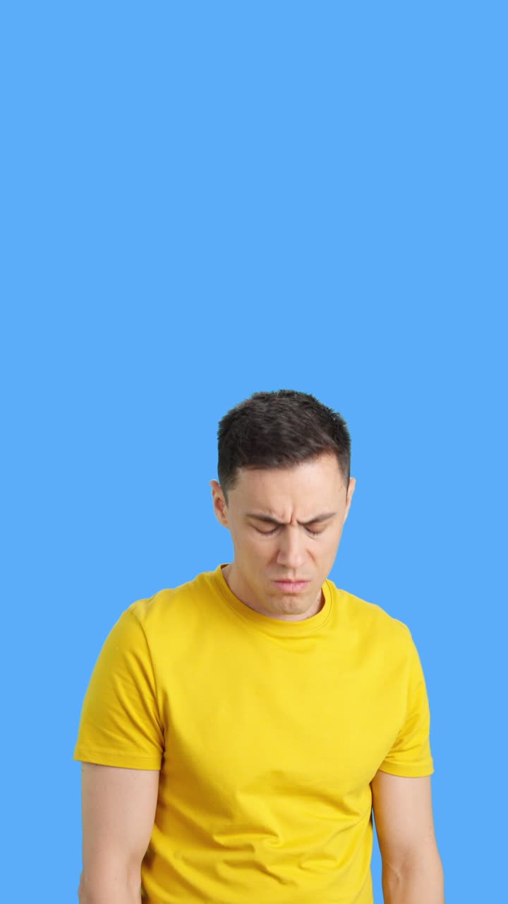 A man in a yellow shirt looks worried against a blue background
