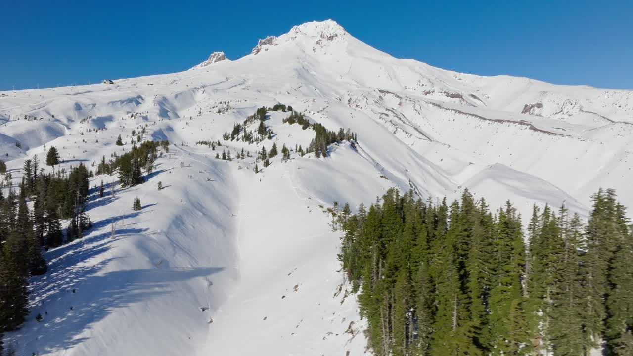 Bidikan drone udara yang mengarah ke Gunung Hood yang tertutup salju dan gletsernya, fumarol, dan jurang di belakang Timberline Resort yang terkenal dekat Portland Oregon saat matahari terbenam di musim dingin dengan pohon pinus