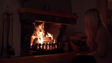 a pretty blonde girl puts a peace of wood into the fire