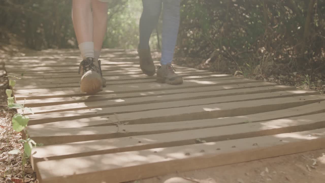 Low section of african american couple hiking on boardwalk in forest, slow motion
