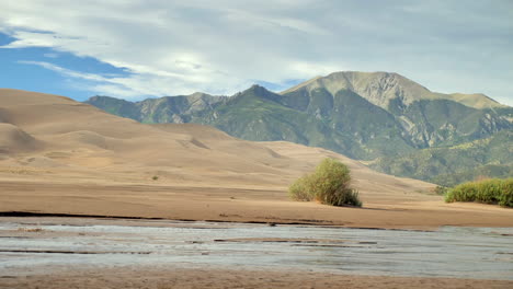 Agua-De-Río-Que-Corre-A-Través-Del-Desierto-Con-Cordillera-En-Grandes-Dunas-De-Arena-Colorado