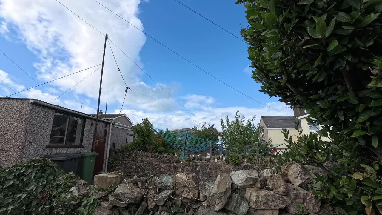 Time lapse sunset clouds passing over rural Welsh cottage stone garden wall with windy trees foliage