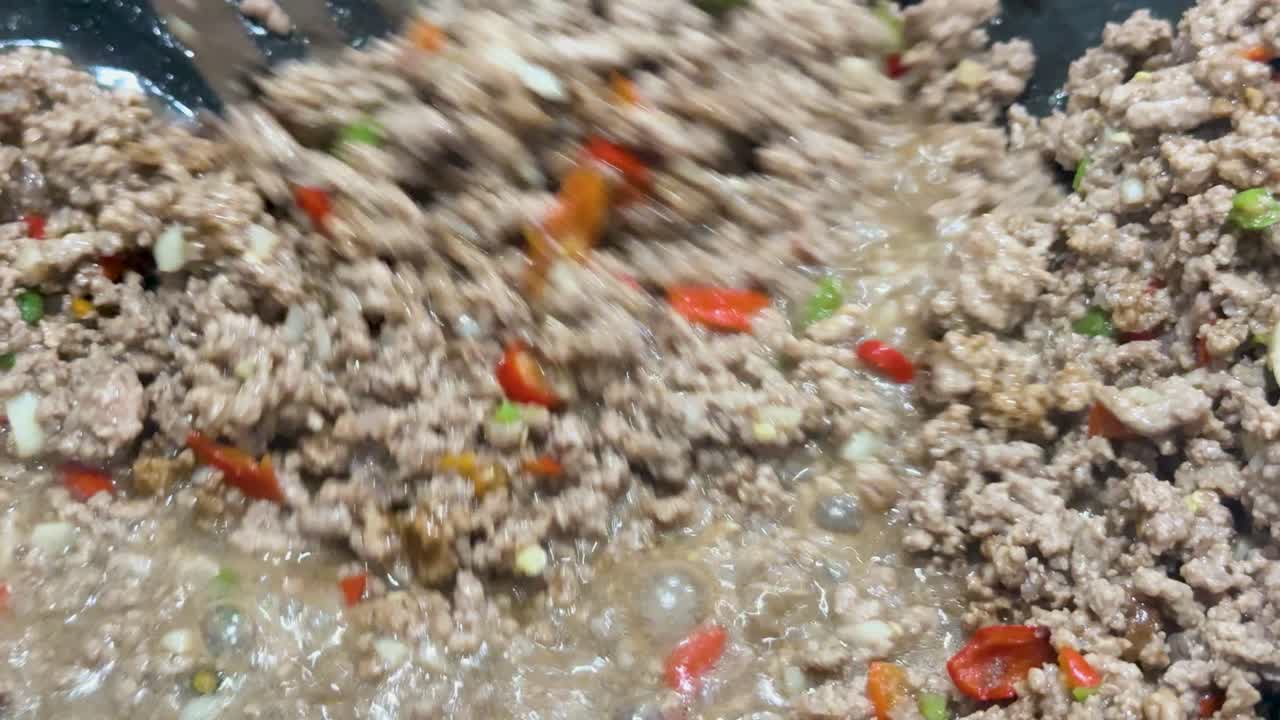 Ground pork, chili peppers, and herbs are stir-fried in a hot wok under bright lighting, with dynamic spatula movement and close-up camera angles