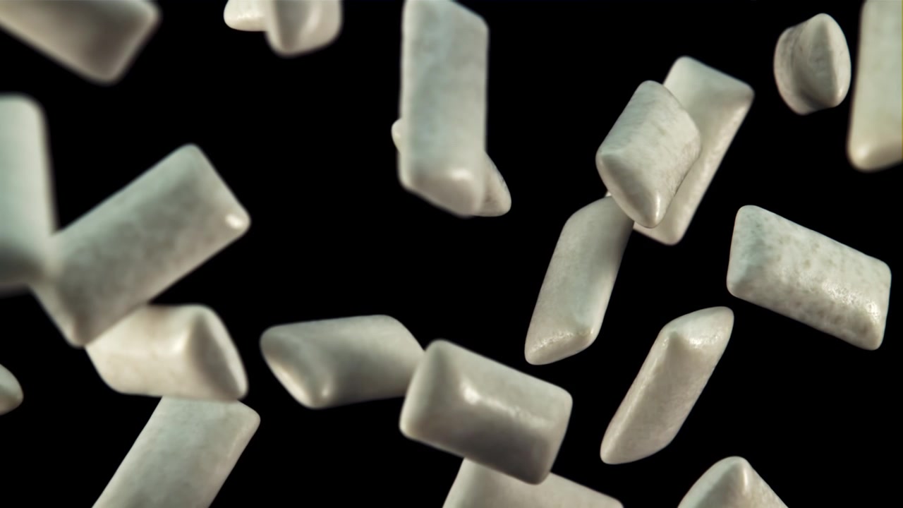 Pezzi di chewing gum bianchi che cadono al rallentatore su sfondo nero.