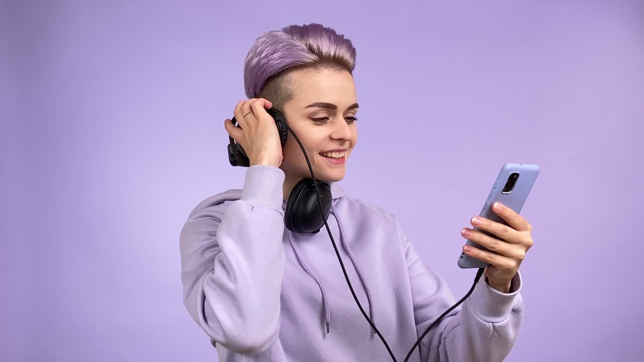 Young woman in all purple listening music via smartphone headphones