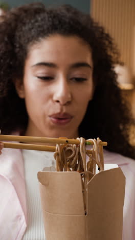 young woman eating noodles with chopsticks from a takeout box