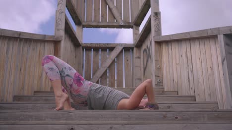 Caucasian-woman-comes-out-of-yoga-pose-on-stairs-outdoors,-low-angle