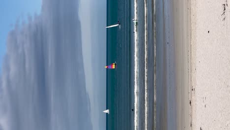 Vertical-Fun-day-at-beach,-sailing-and-surfers