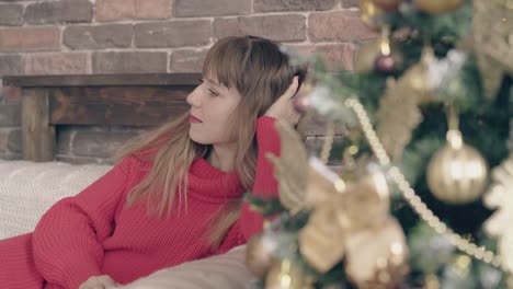 young-fair-haired-girl-dreams-on-couch-near-christmas-tree