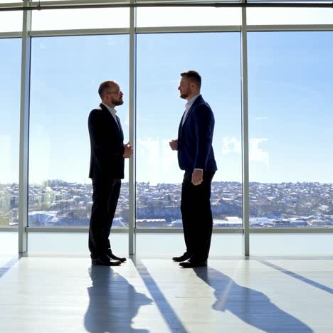 businessman greeting in office. top managers in business suits, shaking hands with each other, against the panoramic window view with a city background
