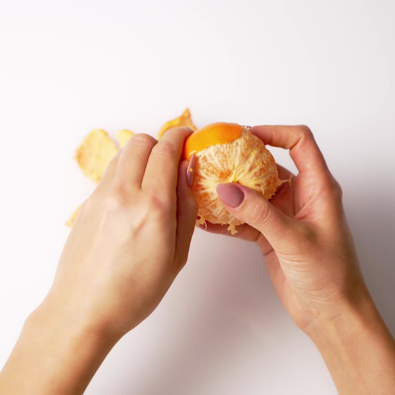 Process of clearance the mandarin. Female's hands cleaning an orange fresh fruit on white background. Top view.