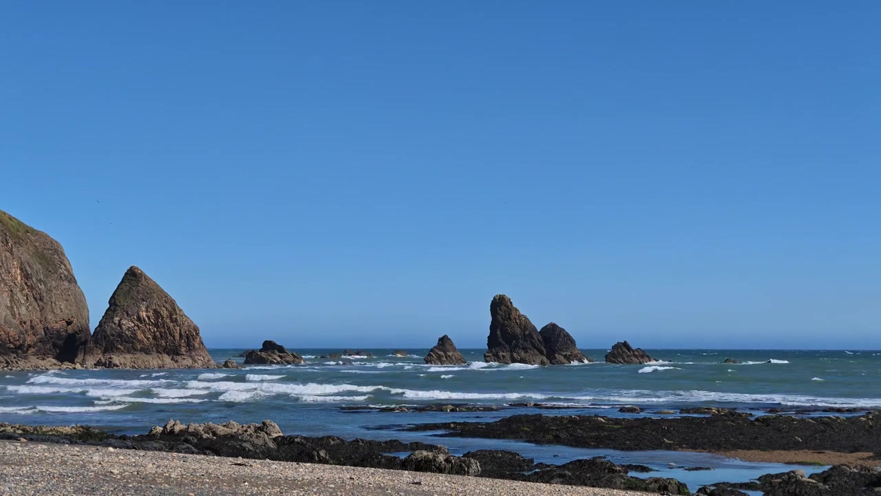 爱尔兰沃特福德海岸线，延时摄影下的蓝天、涌来的海浪、海蚀柱和礁石，留有文案空间。