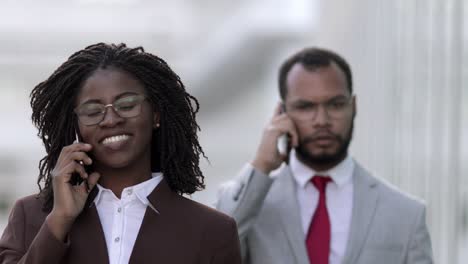 Confident-business-people-talking-on-smartphones-while-walking