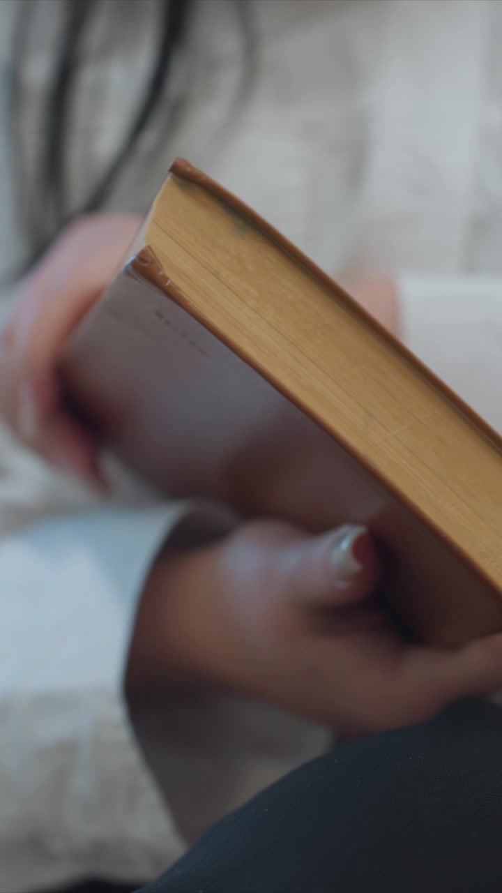 Primo piano di una persona che tiene in mano ed esamina un vecchio libro con pagine usurate. La persona gira il volume con copertina marrone rivelandone la texture invecchiata. Una luce naturale soffusa evidenzia il dorso.
