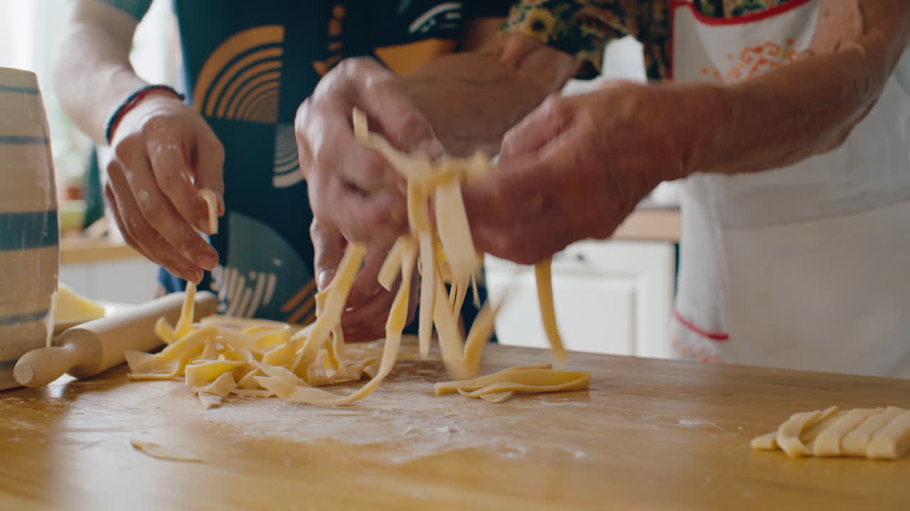 Hands of Family Members Cutting and Separating Fresh Pasta Strips on Table