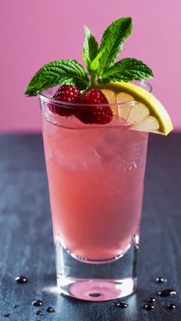 a person garnishes a vibrant pink cocktail with raspberries, lemon, and mint